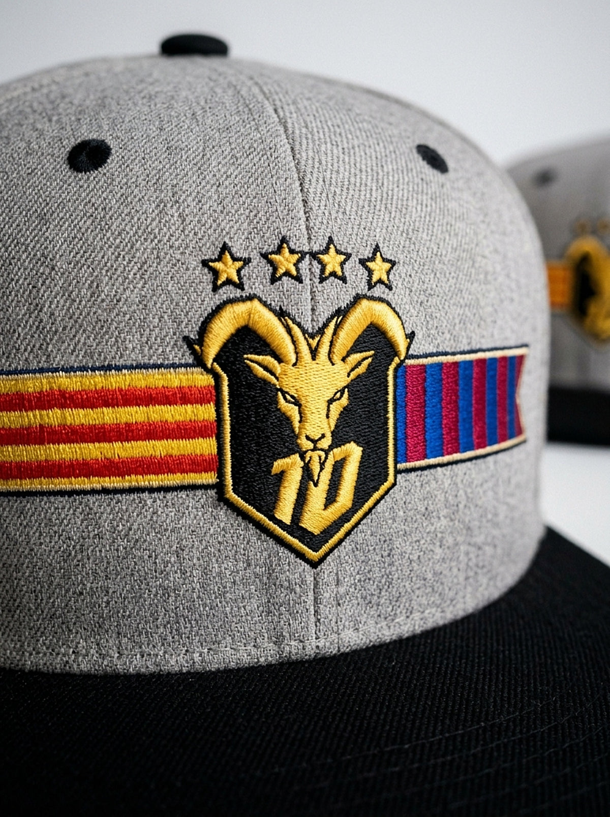 Close-up of the unlimited-colour embroidery on the GOAT Catalan two-tone snapback in Ntụ Gray / Oji Black — gold goat, No. 10 and the split Senyera and blaugrana banner.