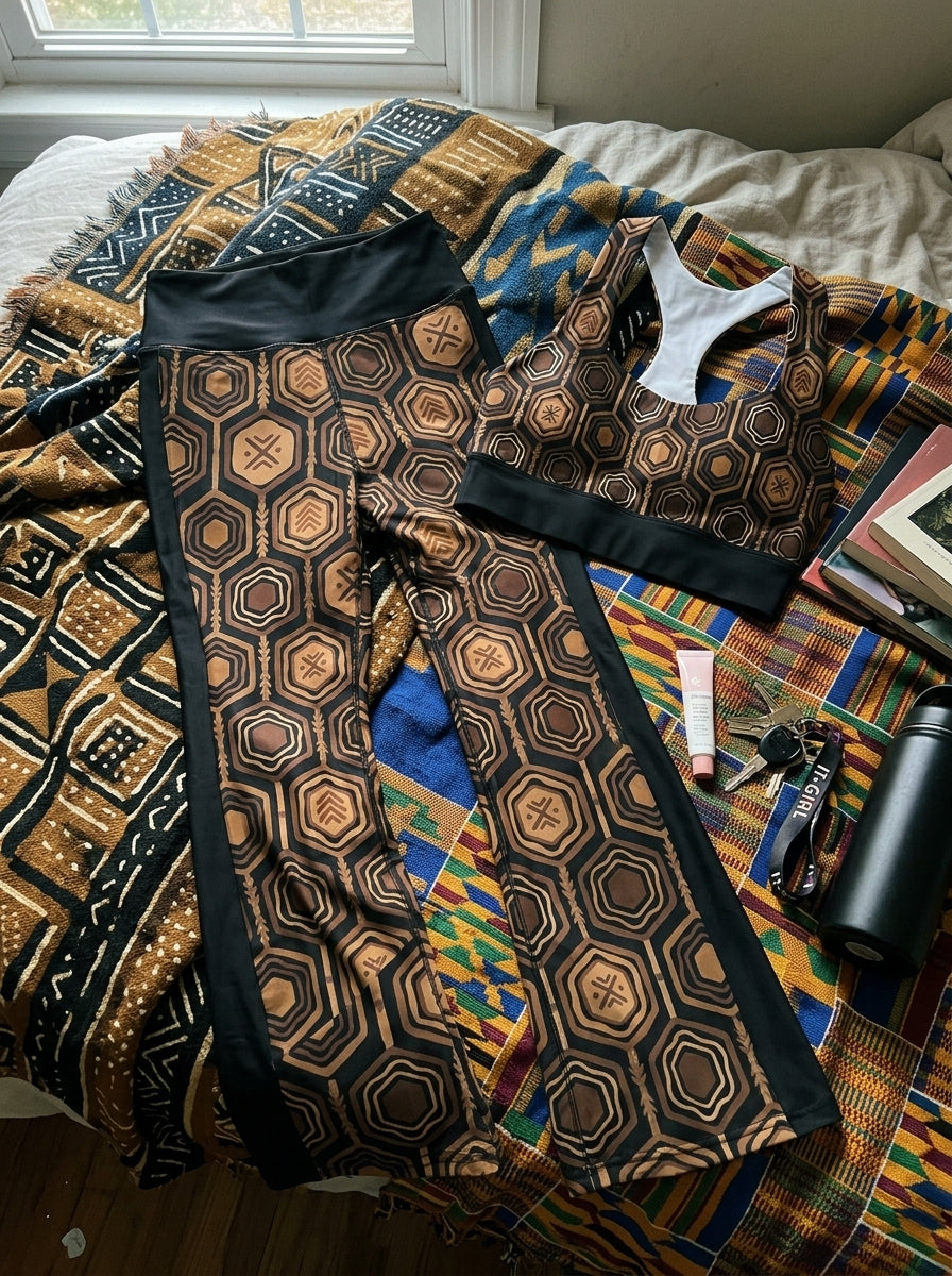 Flat-lay of the Oji Black AnanseNova™ Set — longline sports bra and flare leggings in hexagon print laid on the floor