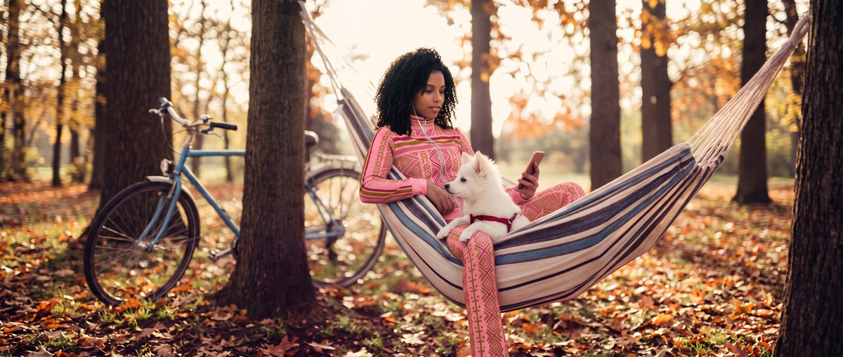 Camila relaxing in a hammock with a white puppy, wearing the N'Donso Adaeze Pink track jacket and flare pants