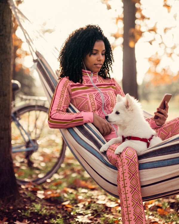 Camila relaxing in a hammock with a white puppy, wearing the N'Donso Adaeze Pink track jacket and flare pants